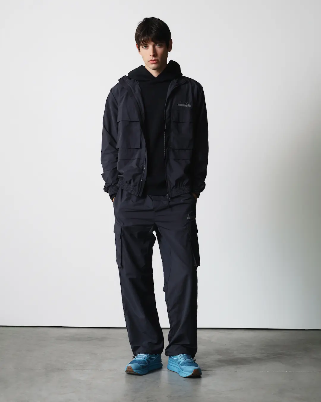 Model in a navy Diadora utility jacket, hoodie and cargo trousers