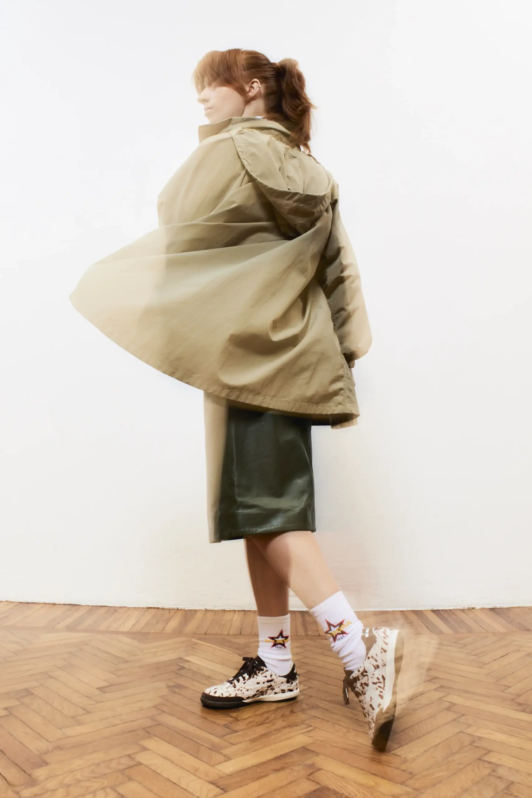 Woman in a khaki parka and olive skirt with star-print sneakers