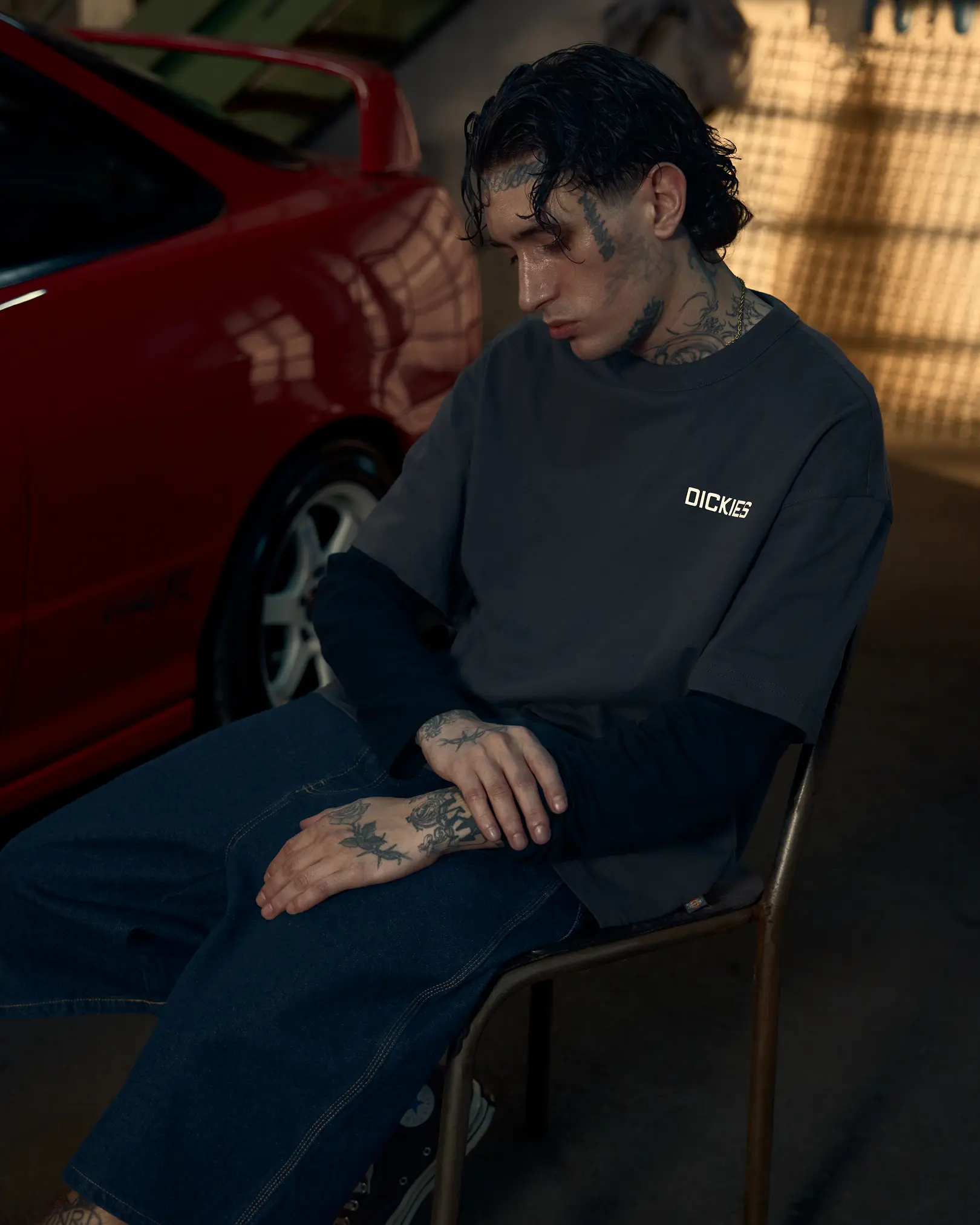 Tattooed man in a Dickies t-shirt seated beside a red car