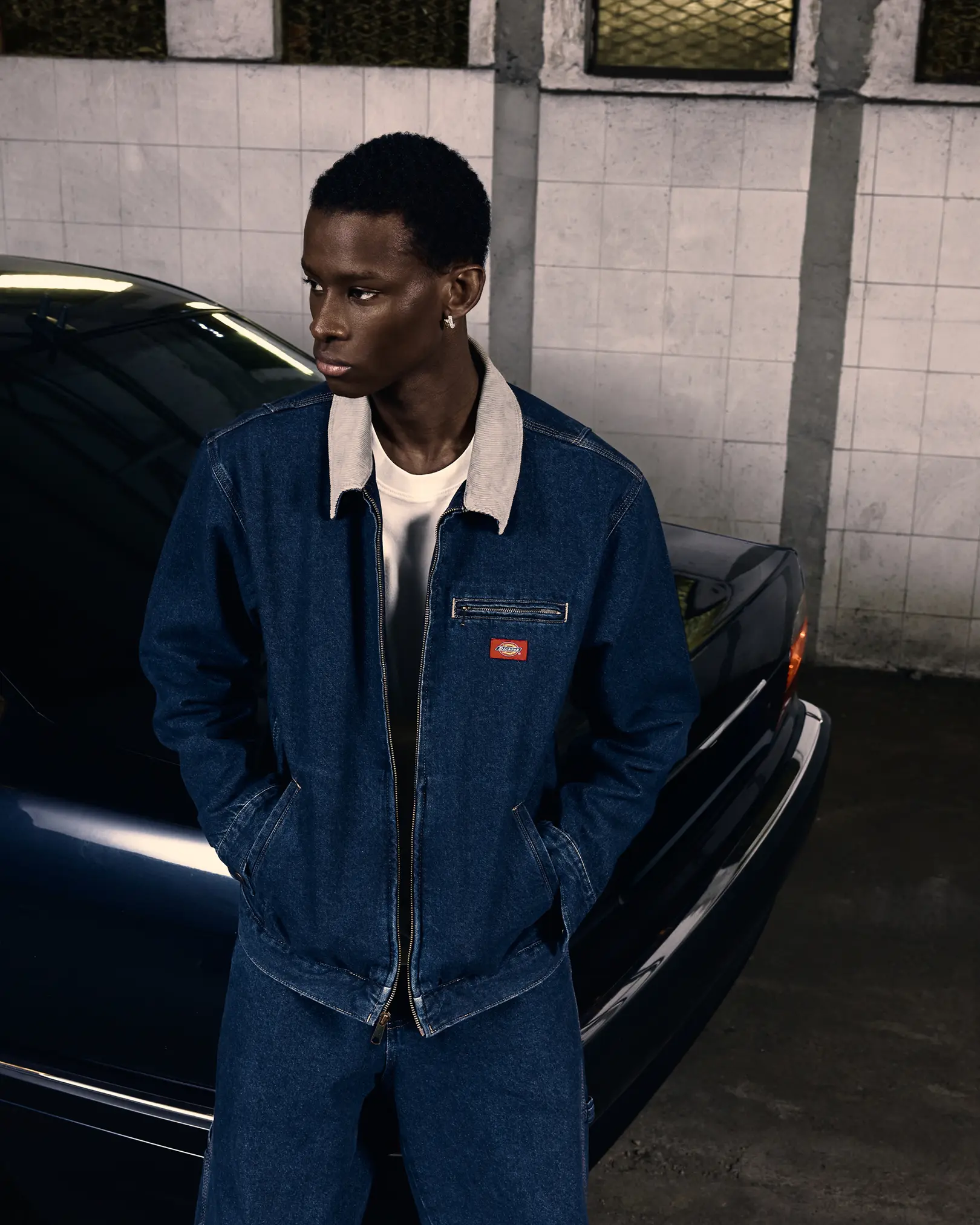 Man in a denim Dickies jacket with a corduroy collar beside a car