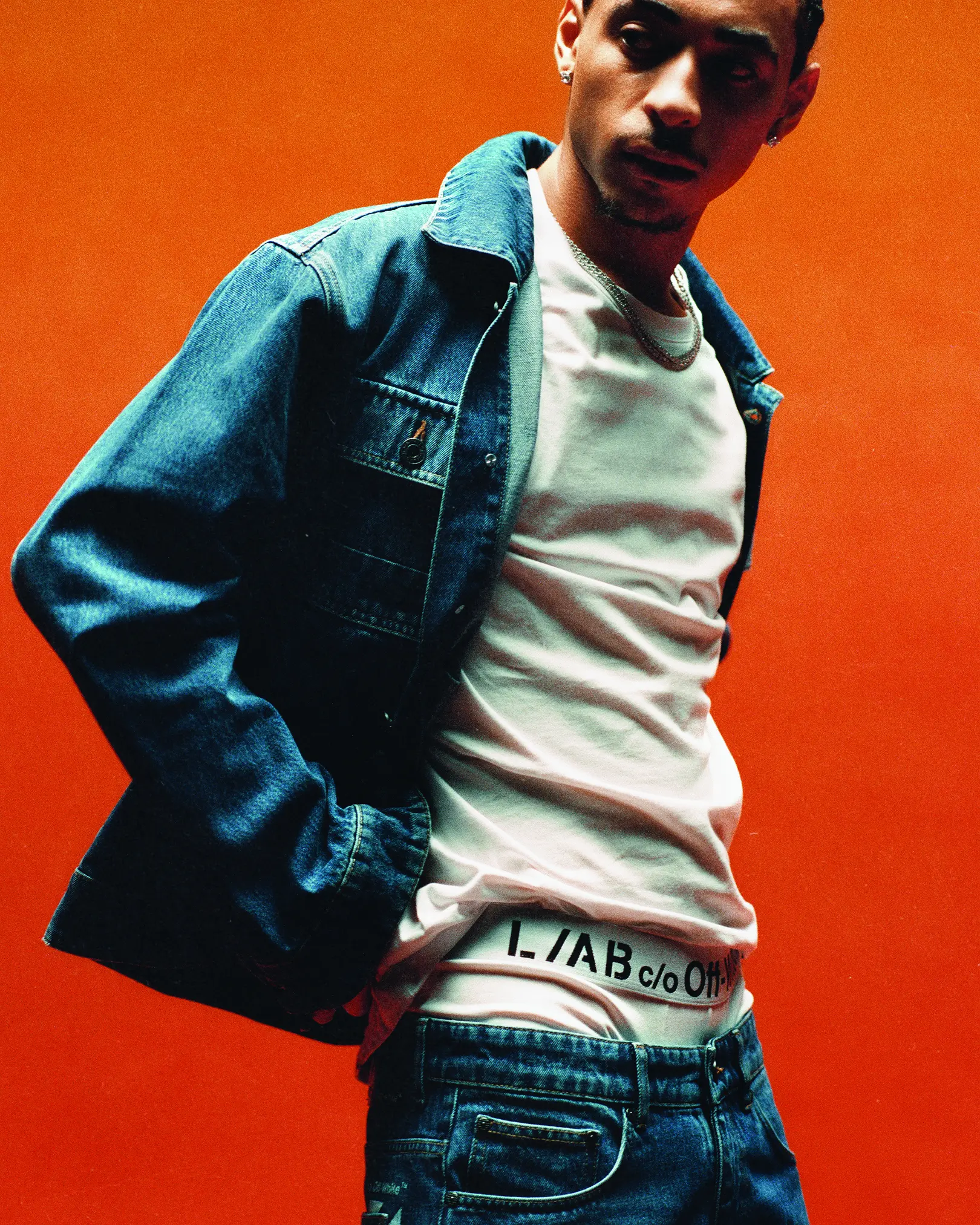 Man in a denim jacket and white tee against an orange backdrop