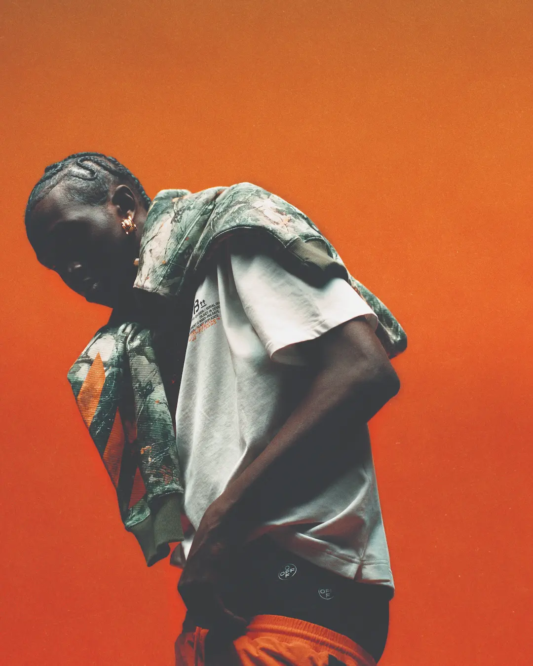 Man in a white tee and camo jacket against an orange backdrop