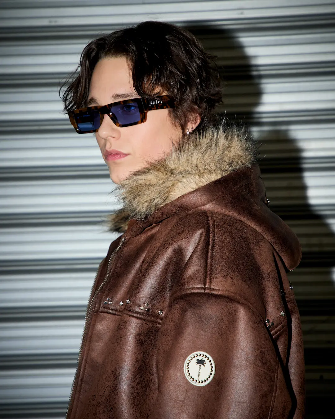 Person in sunglasses and a brown fur-trim leather jacket with a palm patch