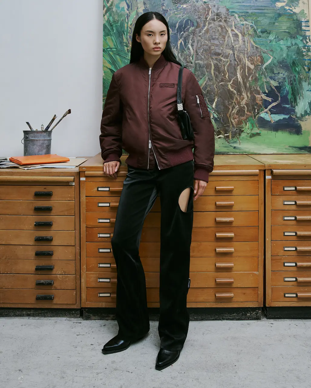 Woman in a burgundy bomber jacket and black trousers in an art studio