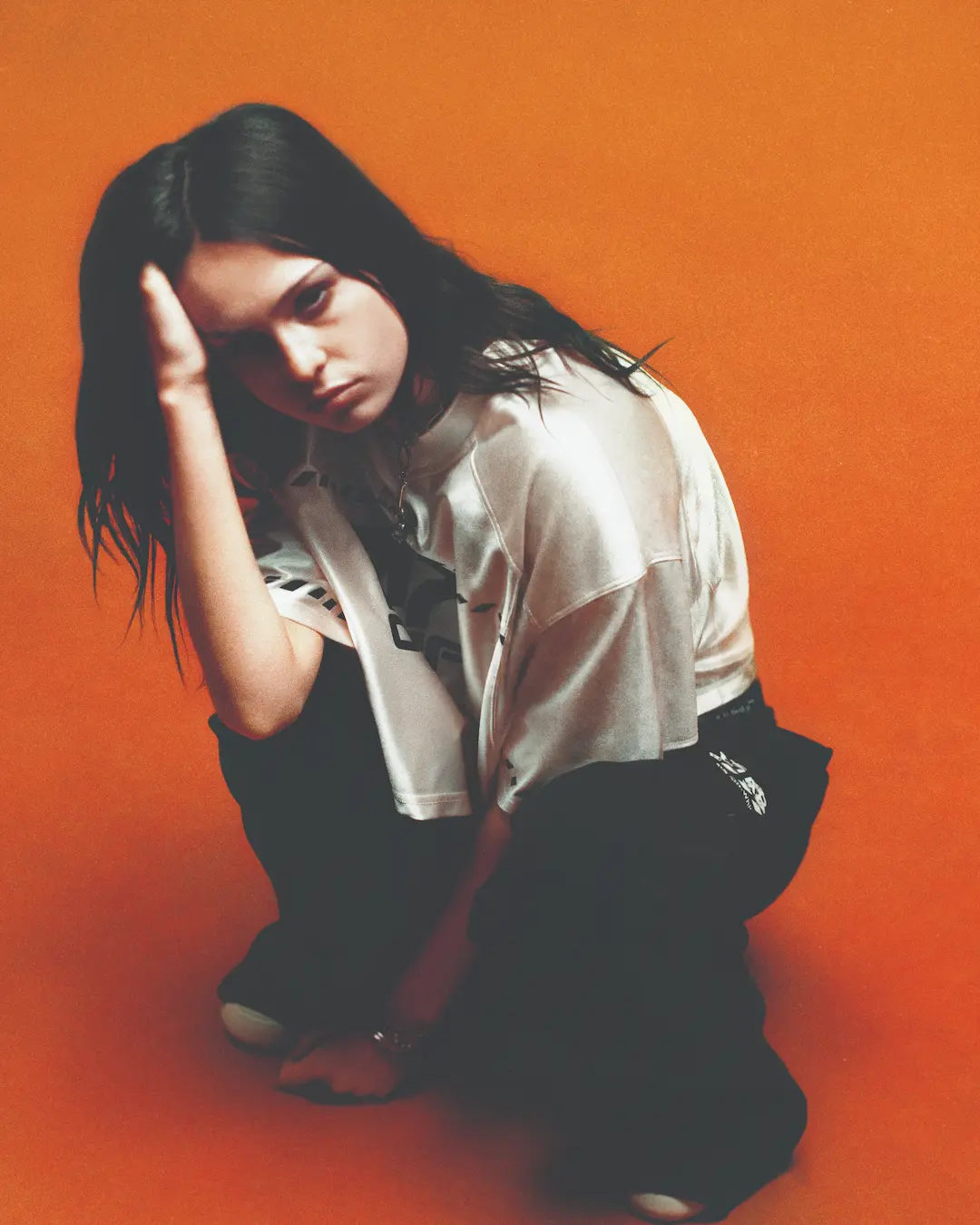 Woman crouching against an orange backdrop in a white tee