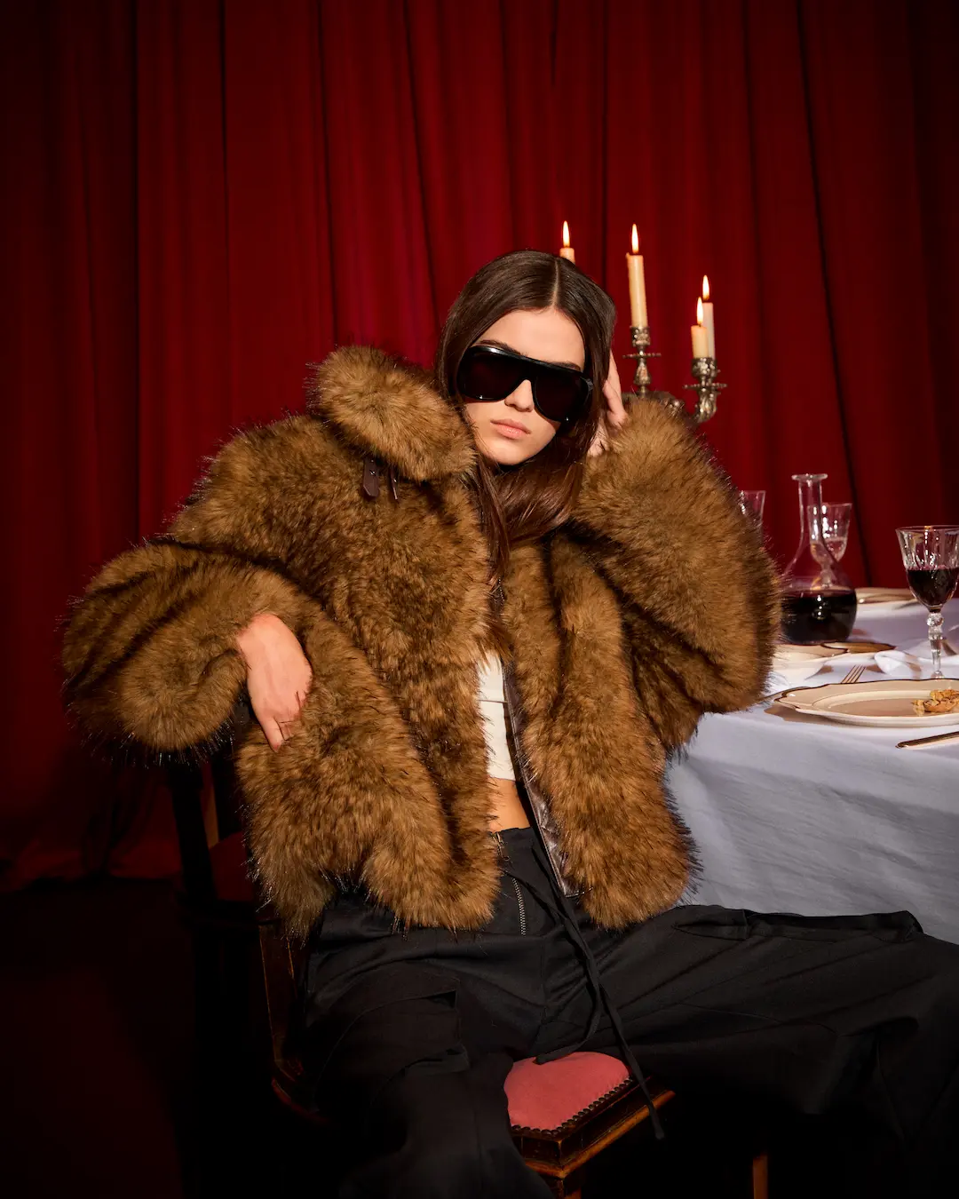 Woman in sunglasses and a brown fur jacket at a candlelit table