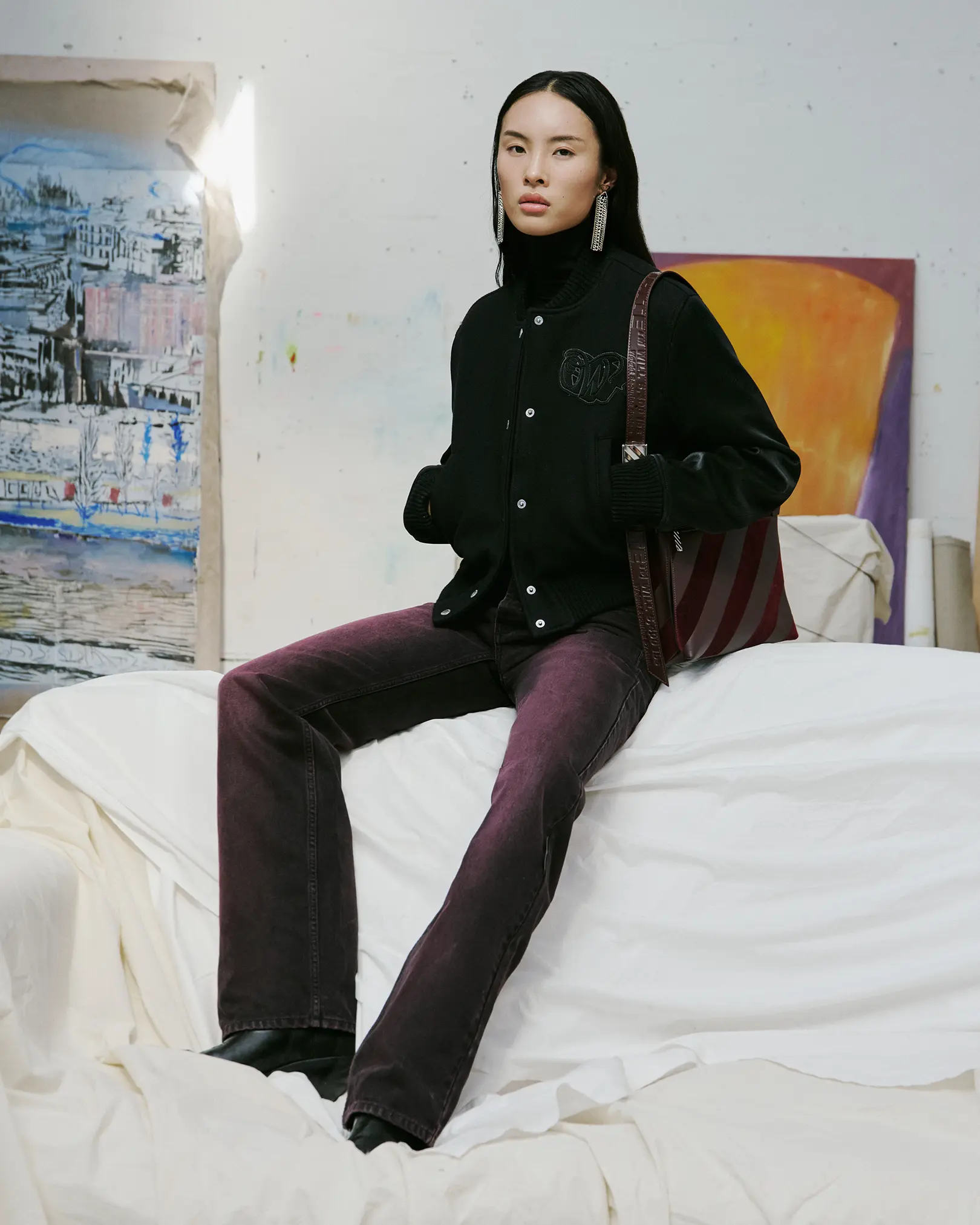Model in a black varsity jacket and plum flared jeans in an art studio