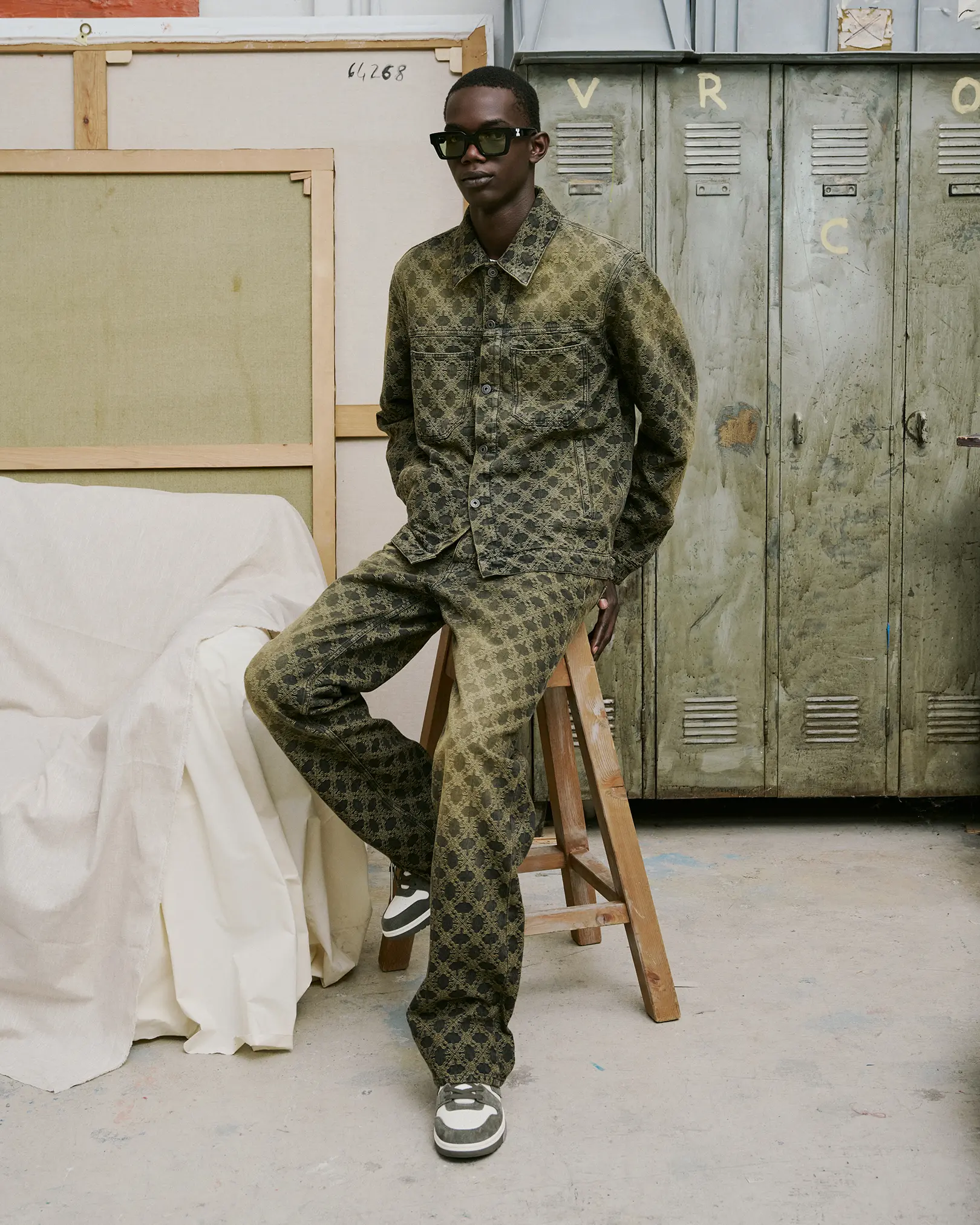Model in an olive monogram-print jacket and trousers on a stool