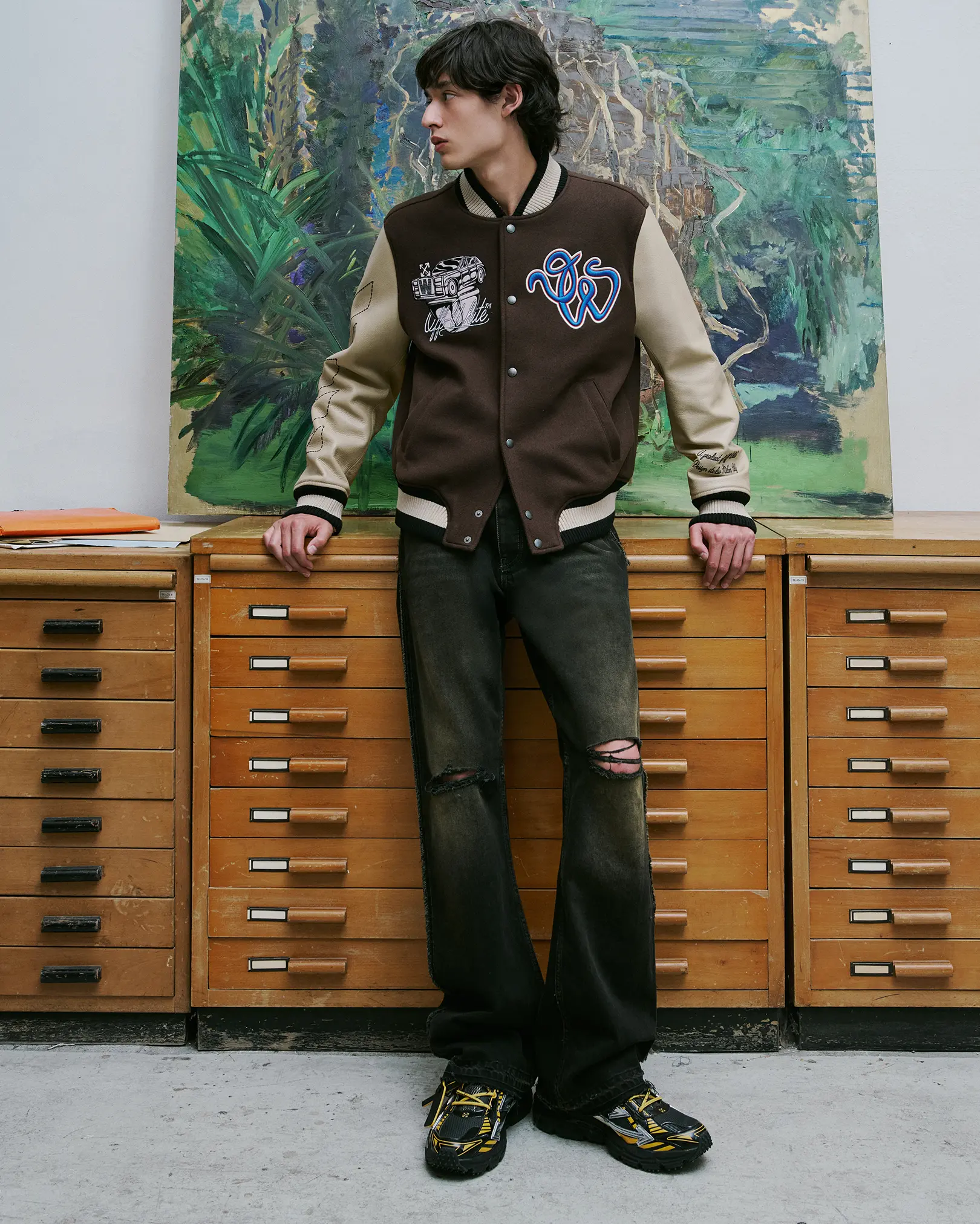 Model in a brown varsity jacket and distressed flared jeans