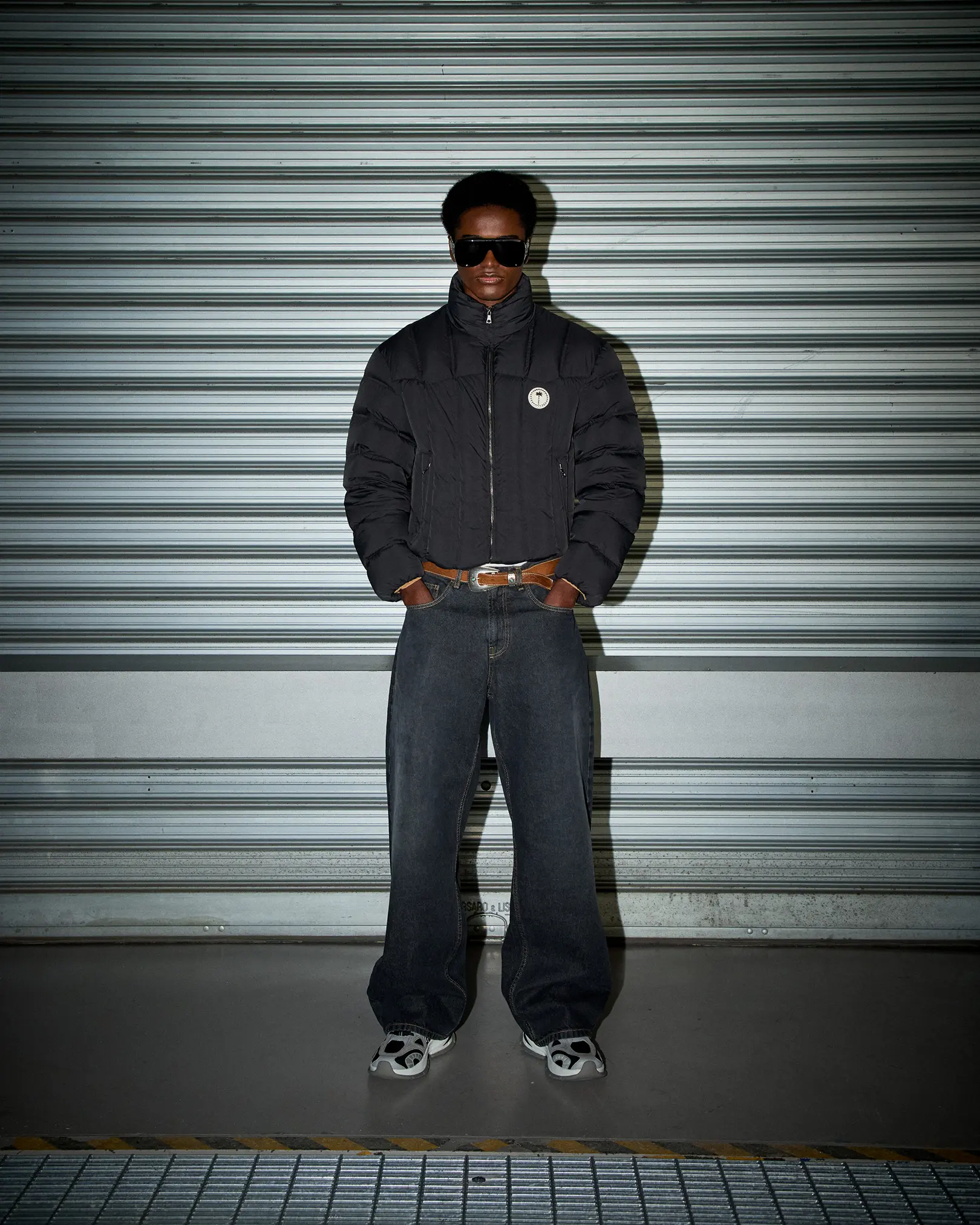 Model in a black puffer jacket and baggy jeans before a metal shutter