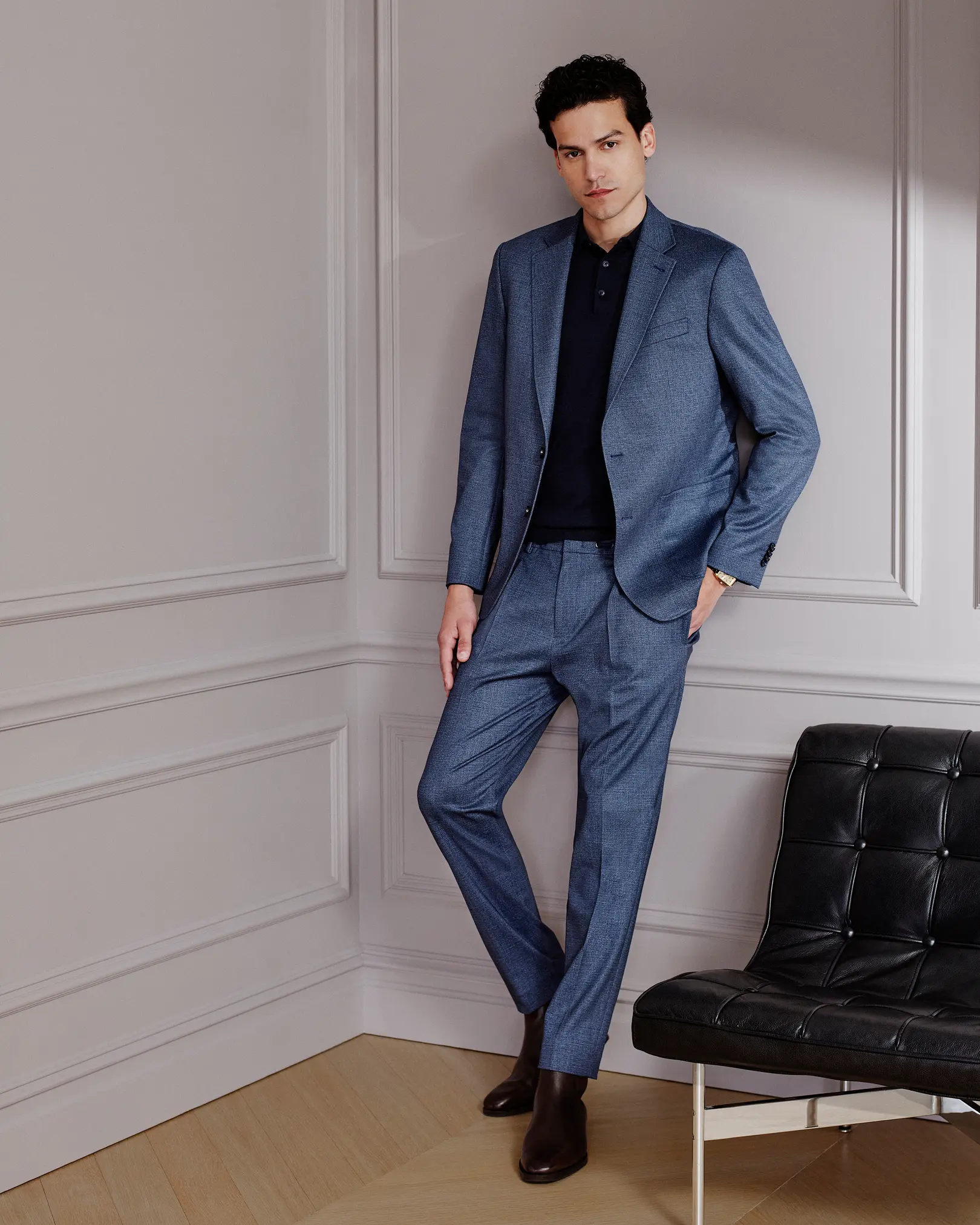 Man in a blue suit and dark polo shirt beside a leather chair
