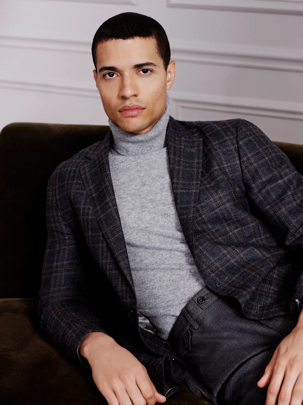 Man in a checked blazer and grey roll-neck on a sofa