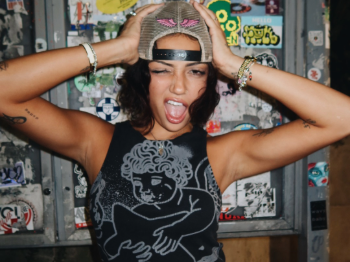 Woman winking with her hands on a backwards cap, wearing a graphic tank top